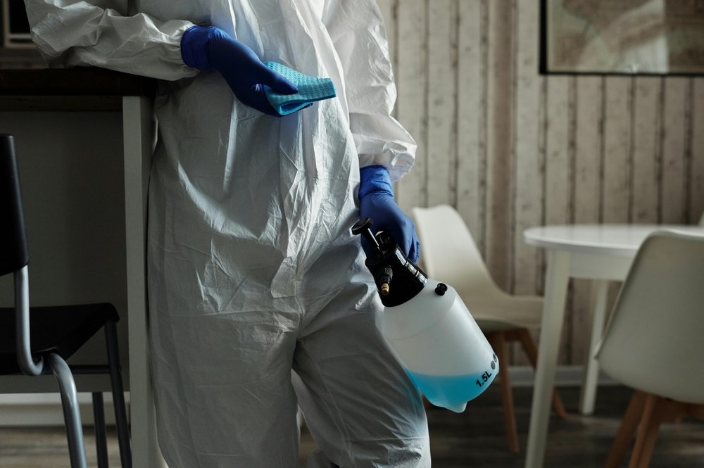 Technician in full PPE with disinfectant sprayer, mid-job