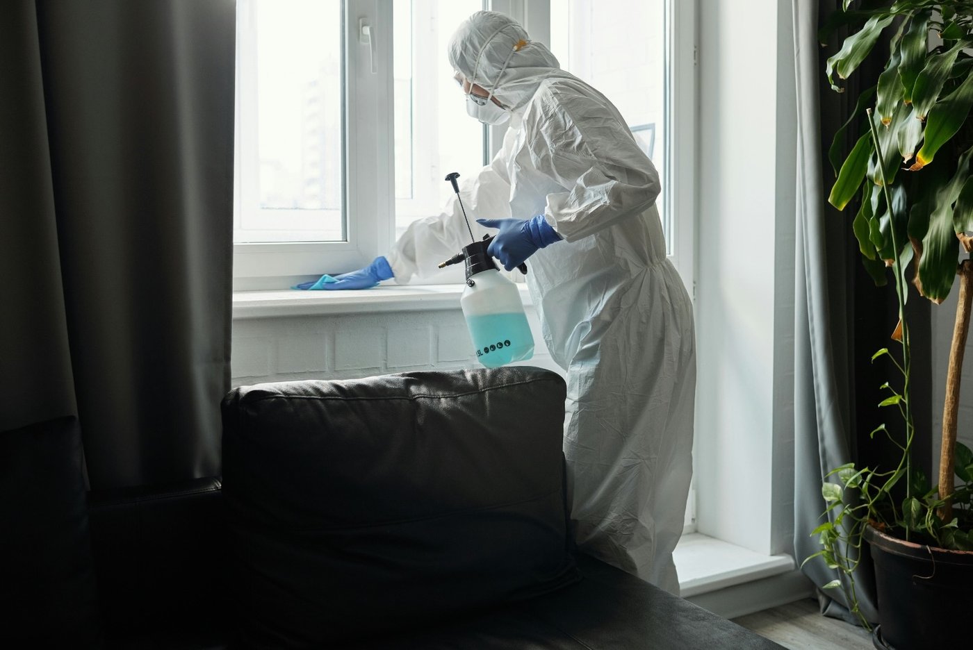 Technician in full PPE decontaminating a window frame
